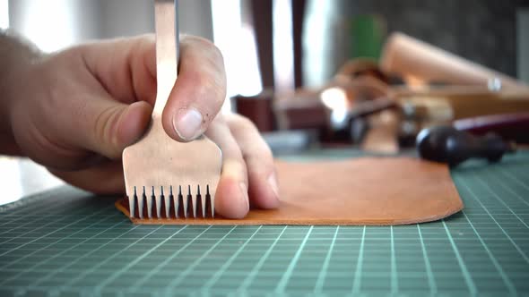 A Man's Hand Holds a Piercer Punches on a Piece of Leather and Punches a Hole with a Hammer