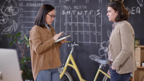 Asian Woman Discussing Work with Colleague in Office