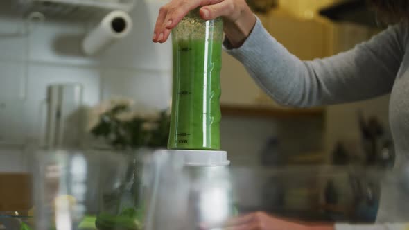 Caucasian woman preparing green vegetable smoothie in kitchen