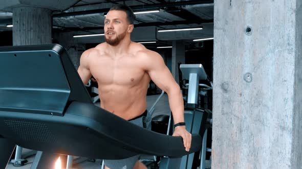 A Bearded Attractive Young Man Bodybuilder Running on the Treadmill with an Effort