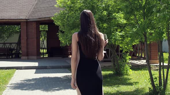 Elegant Woman with Glass of Wine Walking in Garden of Mansion