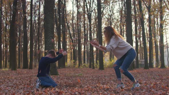 Woman with Leaf and Her Child Boy Making Leaves Fight in Autumn Yard.