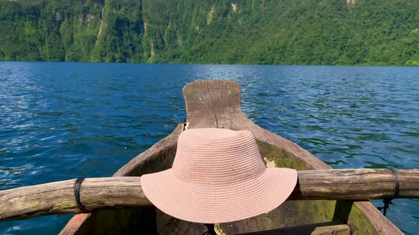 A footage of a single Hat on a wooden boat while on the move with no people, a blue lake and green f