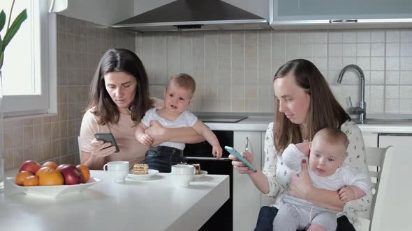 2 mothers with babies use the phone and do not look at each other. Friendly meeting, guests