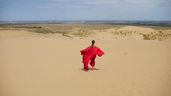 Sexy Brunette Woman in a Red Satin Long Dress Walks on Sand Dunes in the Desert