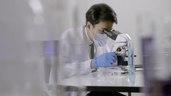 Asian scientist doing some research and looking through a microscope in laboratory.