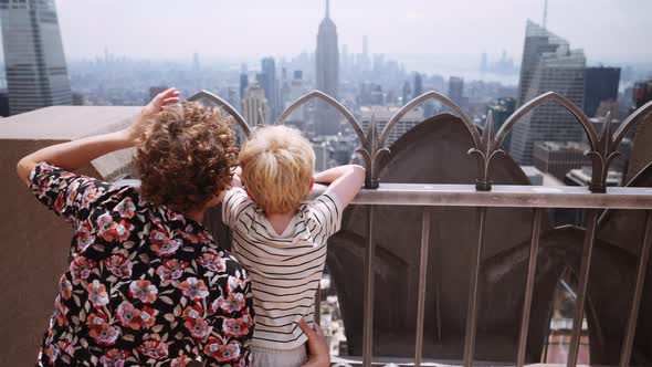 Mother And Boy Looking Over Railings On Rooftop To New York City