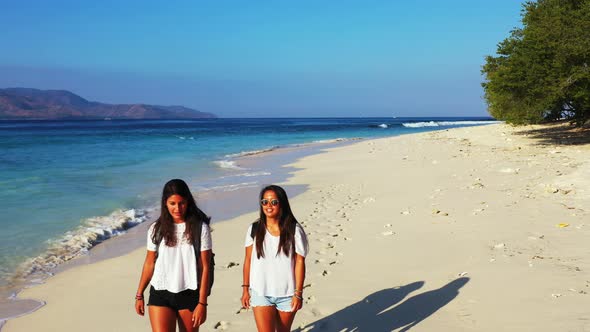 beautiful young women in the white t-shirts walking barefoot on the tropical beach leaving footprint