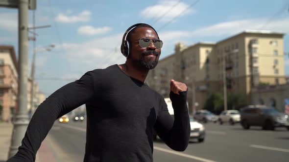 Happy Black Man Is Listening To Music and Singing Walking at Street in Sunny Day