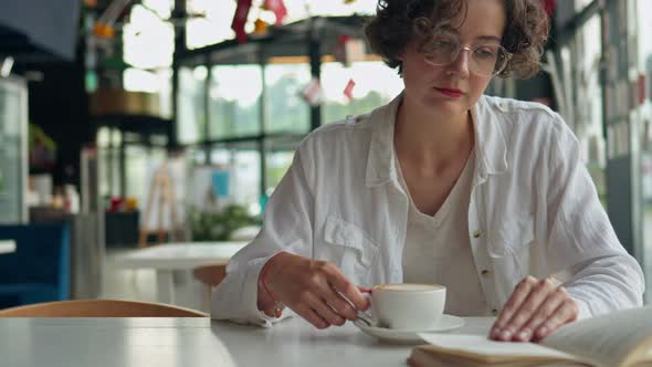 A Young Beautiful Concentrated Girl Restaurant Cafe Drinks Coffee Reads A Book, A Woman Drinks