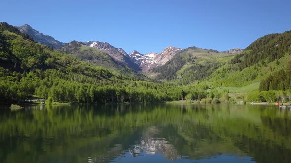 Flying low over lake as green mountain side reflects in the water