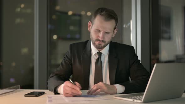 Young Businessman Thinking and Writing Document at Night