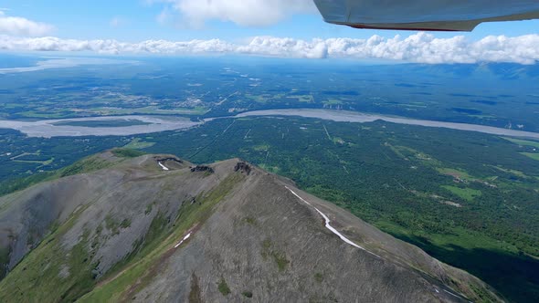 Small airplane flight over a mountain ridge with the town of Palmer Alaska and the Matanuska river i