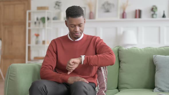 African Man Waiting while Checking Watch on Sofa