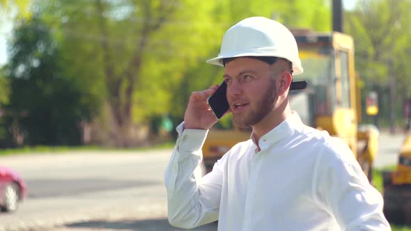 Manager of the Repair Works Against the Background of a Road Construction Site Talking on the Phone