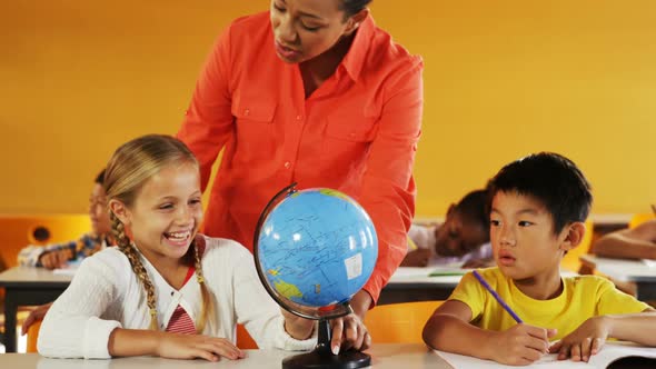 Teacher assisting school kids in reading globe in classroom