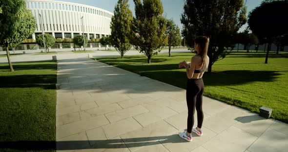 The Girl Looks at Her Smart Watch and the Stadium at Dawn