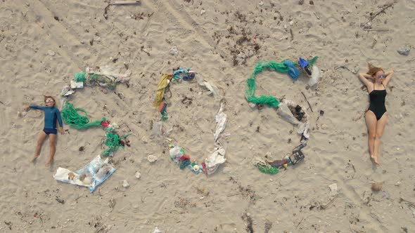 Aerial Shot of the Song SOS Made of Trash on a Beach. A Woman and a Boy Lay By the Sign. Ecological