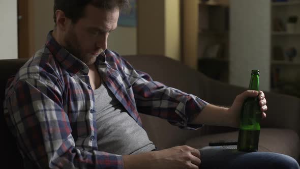 Male Dozing Off on Sofa with Bottle of Beer in Hand, Having Drunken Hiccups