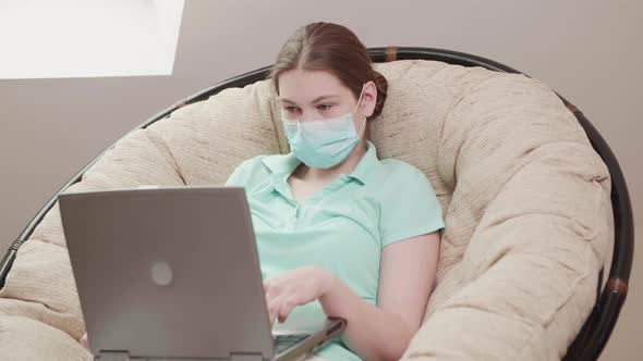 Girl Wears Protective Mask in Coronavirus Pandemic Browsing Internet on Laptop