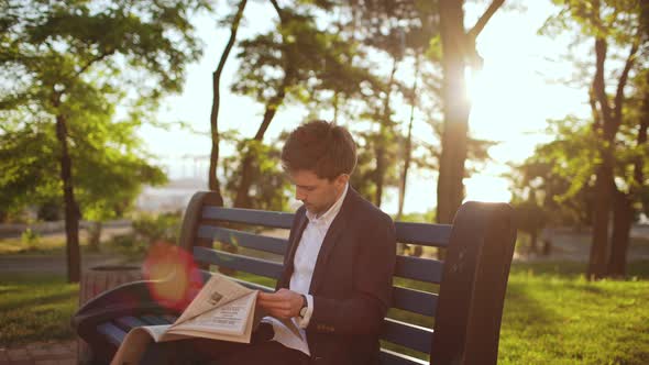 Handsome Business Man Reading Newspaper in Green Park Nature Sitting on Bench in Salesman Suit