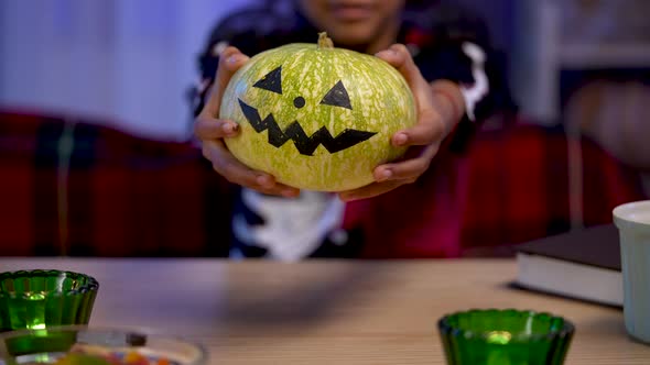 Little African American Girl in Festive Costume is Holding an Pumpkin with Painted Smiling Face