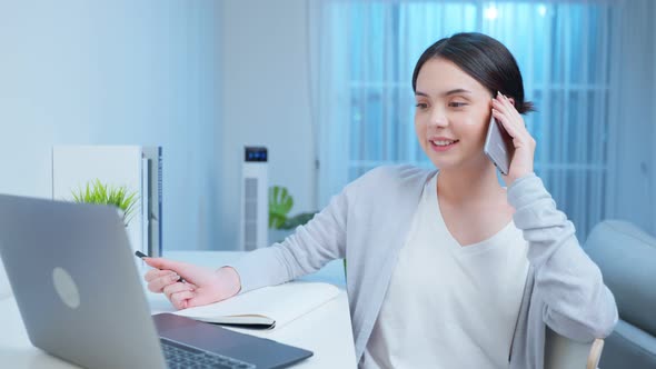 Attractive freelancer girl sit on study table, use mobile phone call for late work meeting at night.