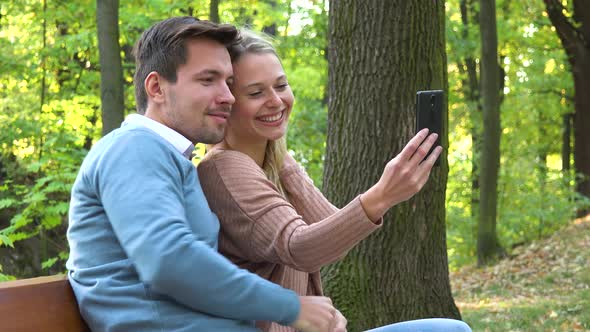 A Young Attractive Couple Take Selfies with a Smartphone in a Park on a Sunny Day