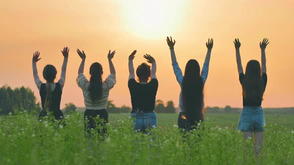 Girls Friends Waving Their Hands to the Setting Sun at Sunset