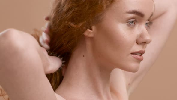 Side View Of RedHaired Female Making Ponytail Over Beige Background