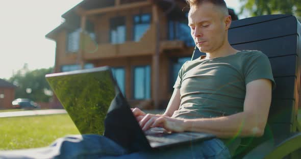 Young Focused Man Working at Laptop in Courtyard of Country House