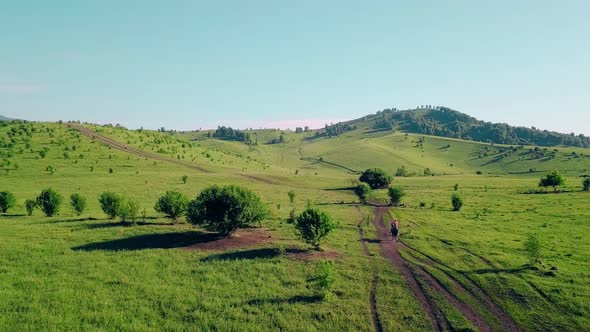 Aerial: Slow Motion: Man with Naked Torso, Moves on Horse, Along Dusty Road, Along Fields and