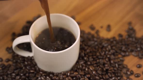 Slow motion coffee pour from french press with coffee beans surrounding mug.