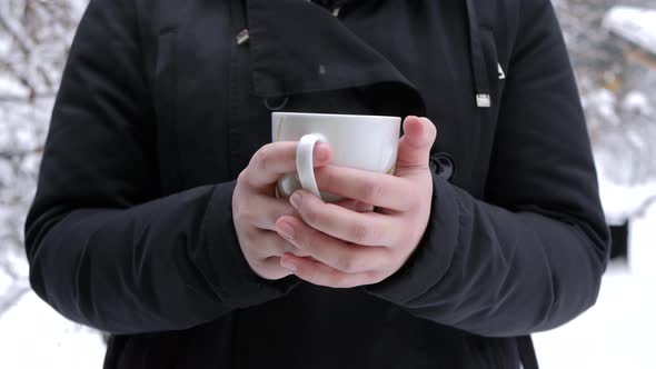 Asian woman warming her hands on a cup of hot tea in winter scenery.