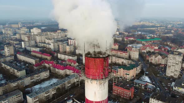 Large red-white industrial chimney with smoke in the city