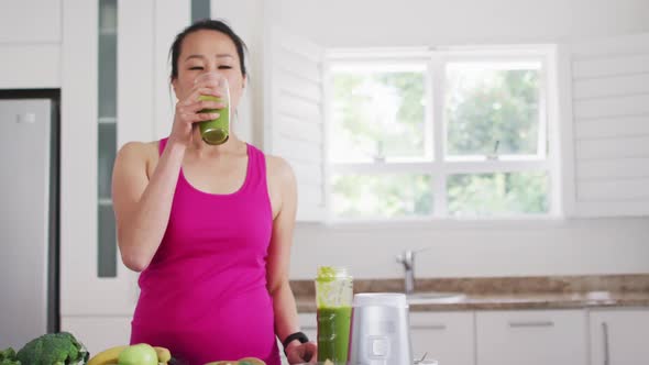 Relaxed asian woman drinking smoothie in kitchen