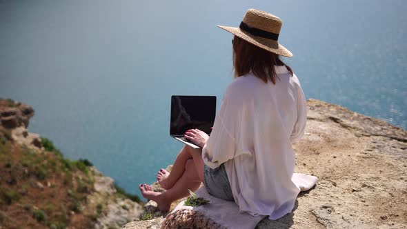 Successful Business Woman in Yellow Hat Working on Laptop By the Sea