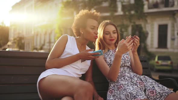 Young Beautiful Girls Speaking Smiling Looking at Phone Sitting in City Park