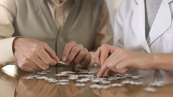 Female Caregiver Helping Aged Man Doing Puzzle Table, Mental Training, Alzheimer