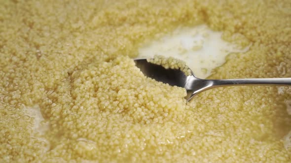 Cooking couscous. Stir grains in water with a spoon