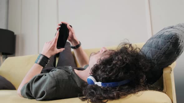 Curly Haired Guy on the Couch Listening Music with Headphones Having Fun