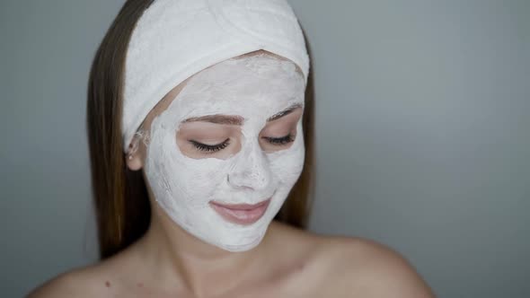 Woman with Cosmetic Mask on Face Looks and Poses at Camera on Neutral Background