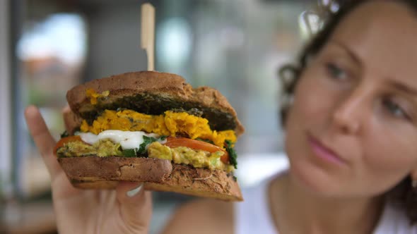 Hungry Young Lady Holding in the Hand and Looking at Her Tasty Vegan Sandwich