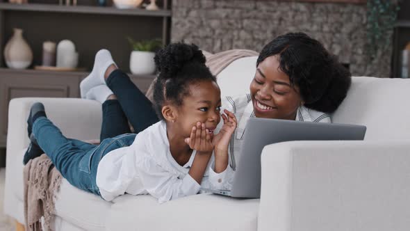 Happy Parent African Mother and Cute Child Daughter Looking at Laptop Screen Talking Having Fun