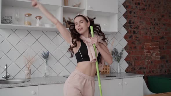 Woman Singing Into Mop While Cleaning Kitchen. Acting Funny During Domestic Chores. Beautiful