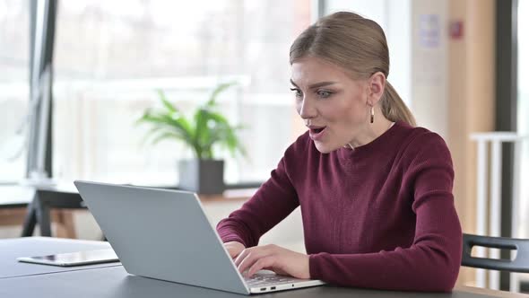 Young Woman Celebrating Success on Laptop in Office