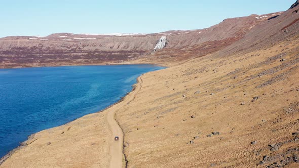 Car On Dirt Track By Fjord Towards Waterfall On Mountain