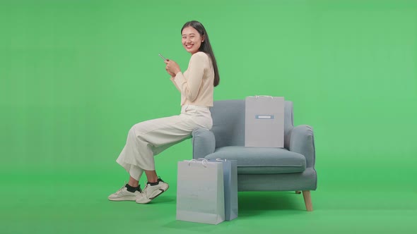 Woman With Shopping Bags Using Mobile Phone Turn To Smile While Sitting On Sofa At Green Screen