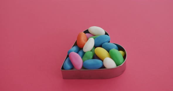 Video of overhead view of multi coloured sweets in heart shape over red background