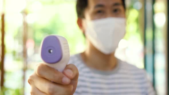 Young Asian Man in Mask Using Medical Digital Infrared Thermometer to Check Body Temperature
